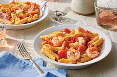 two plates of pasta with shrimp and tomatoes on the table next to a glass of water