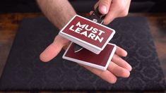 a person holding two small magnets with the words must learn on them in red and white