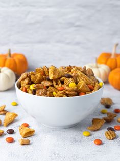 a white bowl filled with candy cornflakes next to pumpkins and gourds