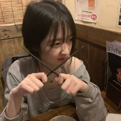 a woman sitting at a table with chopsticks in front of her face