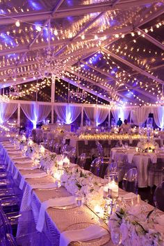 a banquet hall with tables and chairs covered in white linens, lit by fairy lights