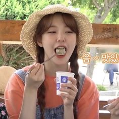 a young woman is eating from a cup and holding a spoon in her hand while wearing a straw hat