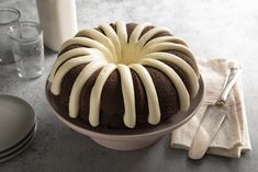 a chocolate bundt cake with white icing sitting on a table next to plates and utensils