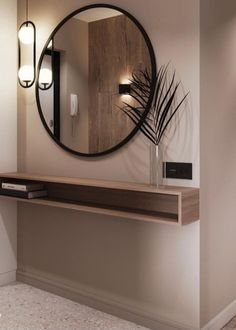 a round mirror hanging on the wall above a wooden shelf with a plant in it