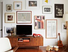 a living room filled with furniture and lots of framed pictures on the wall above a flat screen tv