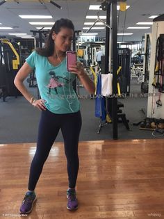 a woman standing in a gym holding a cell phone