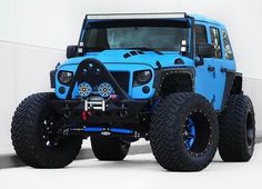 a blue jeep is parked in front of a white wall with black rims and tires