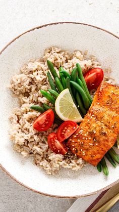 a white bowl filled with rice, green beans and salmon on top of a table