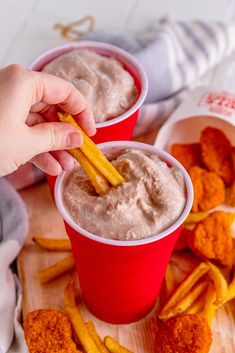 two red cups filled with dip and french fries on top of a wooden cutting board