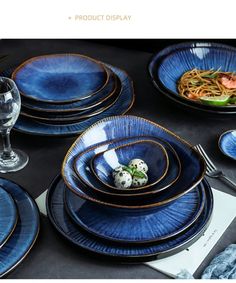 blue dishes with gold rims are arranged on a black tablecloth and place settings