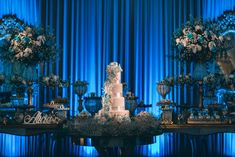 a white wedding cake sitting on top of a table with blue drapes behind it