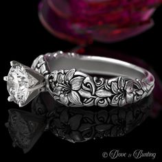 a close up of a ring with a flower design on the side and a diamond in the middle