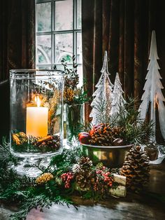 a table with candles, pine cones and evergreens on it in front of a window