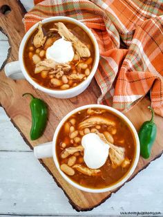 two white bowls filled with chili and beans on top of a cutting board next to a green pepper