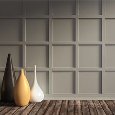 three vases sitting on top of a wooden floor in front of a gray wall