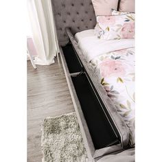 a bed with pink flowers on it and a black drawer under the headboard is in front of a window