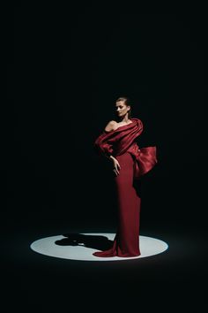 a woman in a long red dress standing on a white circle with her hands behind her back