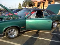 a green car parked in a parking lot next to another car with its hood open