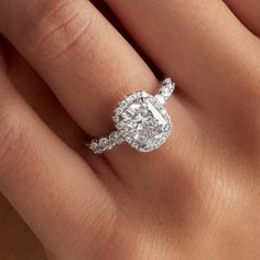 a woman's hand with a diamond engagement ring on her left hand and the center stone is surrounded by diamonds