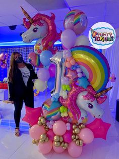 a woman standing next to a giant unicorn balloon sculpture in a room filled with balloons