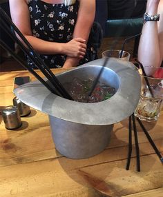 a woman sitting at a table with chopsticks in a bucket filled with liquid