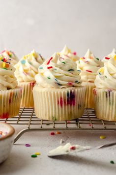 cupcakes with white frosting and sprinkles on a cooling rack