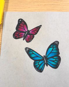 two blue and pink butterflies sitting on top of a piece of paper next to a yellow marker