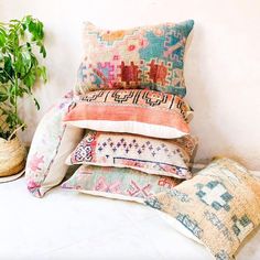 a pile of pillows sitting on top of a white floor next to a potted plant