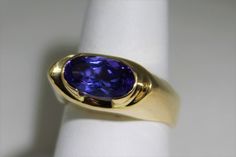 Wow--WOW--TANZANITE This is a eye catching genuine Tanzanite ring. We set this 3.5 carat oval across the finger and it is gorgeous. The 3.5 carat stone is a deep purple with blue overtones ,a choice stone. The stone is 20 mm long and 9 mm wide and is set with bezel ends . This protects the stone from damage. I call the my saddle style ring with a European style shank. the squared bottom keeps the top form spinning over. Currently a size 6 it can be size up or down 1 size, please inquire about pr Modern Oval Tanzanite Sapphire Ring, Oval Amethyst Ring In 14k Gold With Brilliant Cut, Modern Oval Tanzanite Ring, Mens Gemstone Rings, Celebrity Engagement Rings, Tanzanite Ring, Custom Ring, European Style, Custom Rings