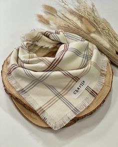 a white and brown plaid scarf sitting on top of a piece of wood next to dry grass