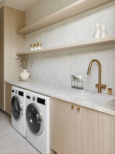 a washer and dryer in a room with white tile on the walls, shelves above