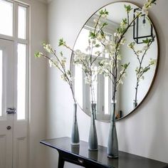 three vases with flowers sit on a table in front of a large round mirror