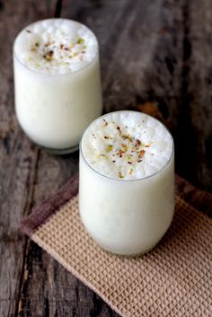 two glasses filled with white liquid sitting on top of a wooden table next to each other