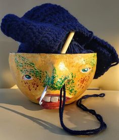 a yellow bowl with a face painted on it and a crochet hook in the middle