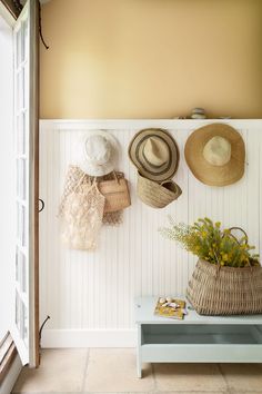 hats are hanging on the wall next to a bench with flowers and baskets in it