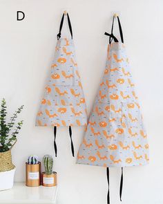 two aprons are hanging on the wall next to a potted succulent