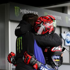 two motorcycle riders hugging each other in front of a building with monster logo on it