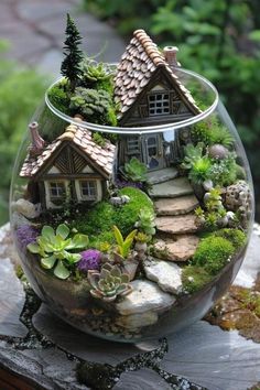 a glass bowl filled with lots of plants and small houses in the middle of it