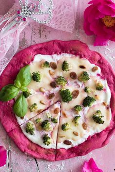 a pizza topped with broccoli and cheese on top of a pink plate next to flowers