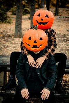 two people sitting on a bench with pumpkins on their heads and one person holding the other's head