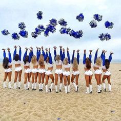 a group of cheerleaders standing on top of a sandy beach under blue pom - poms