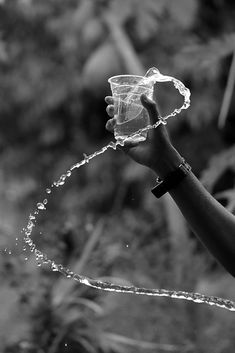 a person is holding a glass with water coming out of it and spraying it onto the ground