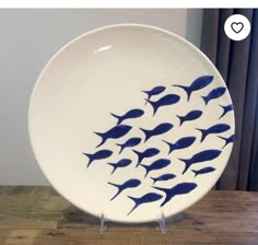 a white plate with blue fish on it sitting on a wooden table next to a window