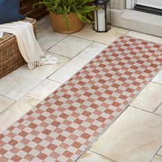 a red and white checkered rug sitting on the ground next to a potted plant