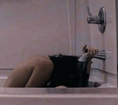 a woman laying down in a bathtub with her head under the faucet