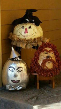 three pumpkins with faces painted on them sitting next to each other in front of a house