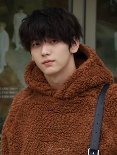 a young man wearing a brown coat and holding a black bag in front of him