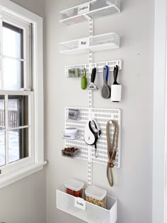 a white wall mounted shelf with scissors and other items on it next to a window