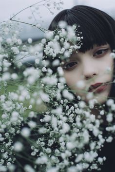 a woman with black hair and bangs is surrounded by white flowers in the foreground