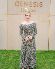 a woman standing in front of a sign wearing a floral dress and pink heels with her hands on her hips